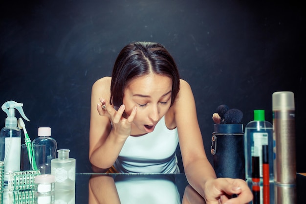 Mujer de belleza aplicando maquillaje. Hermosa chica mirando en el espejo y aplicando cosméticos con un delineador de ojos. Modelo caucásico en el estudio