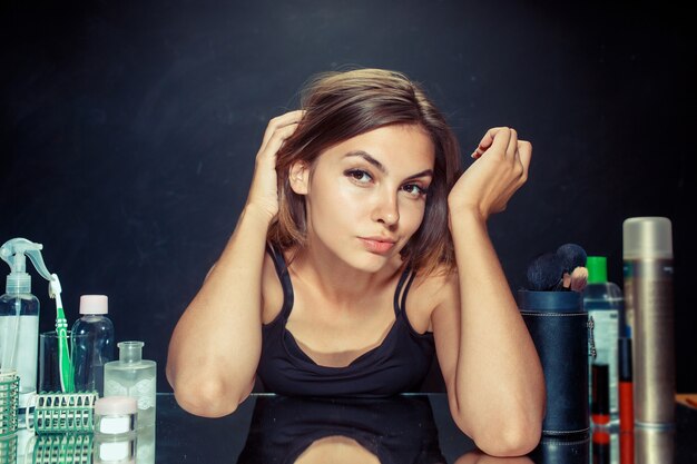 Mujer de belleza después de aplicar el maquillaje. Hermosa chica mirando en el espejo. Mañana, maquillaje y concepto de emociones humanas. Modelo caucásico en el estudio