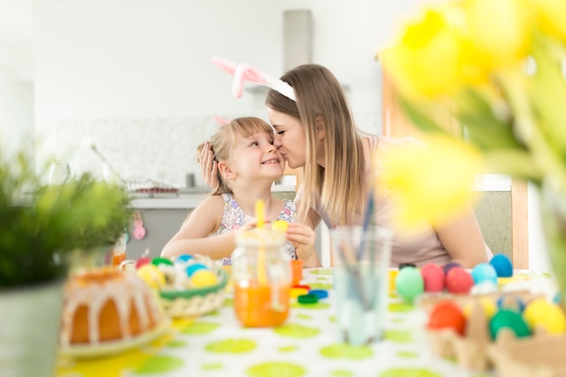 Mujer besando a hija decorando huevos de Pascua
