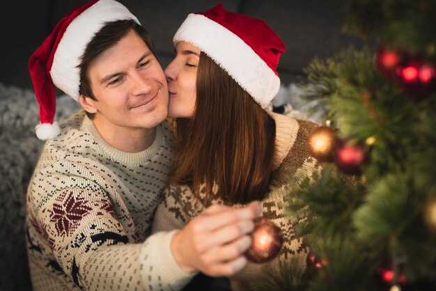 Mujer besando a hombre decorando el árbol de navidad