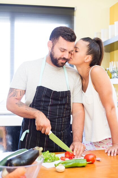 Mujer besando a su marido mientras corta verduras