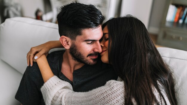 Mujer besando a su novio sentado en el sofá