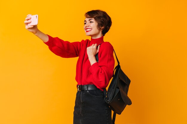 Mujer bien vestida con mochila tomando selfie