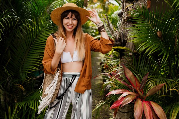 Mujer bien vestida en perfecto estado de ánimo posando juguetonamente en un jardín tropical.