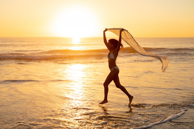 Mujer en bikini corriendo con bufanda en la playa