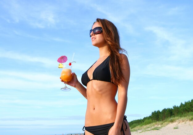 Mujer en bikini en la playa con cóctel fresco de verano