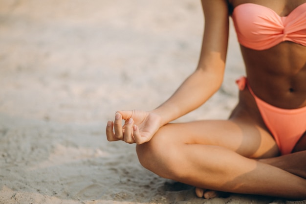 Mujer en bikini practicando yoga en la playa