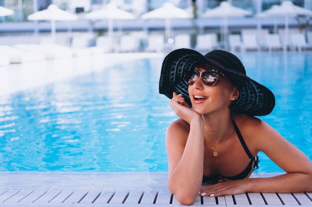 Mujer en bikini con sombrero junto a la piscina