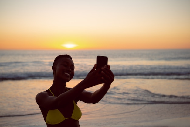Mujer en bikini tomando selfie con teléfono móvil en la playa