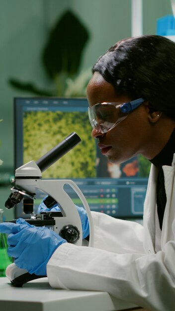 Mujer bióloga mirando la muestra de prueba bajo el microscopio trabajando en el experimento gmo