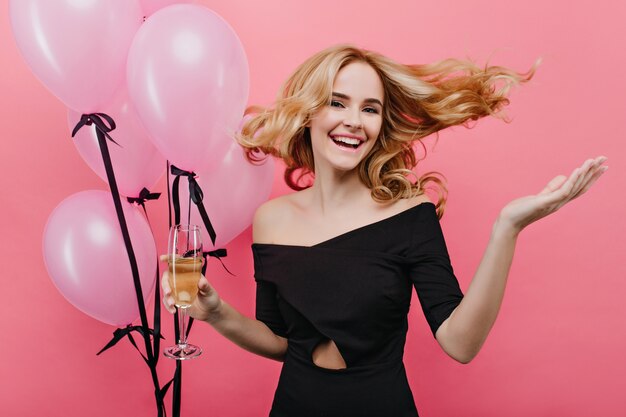 Mujer blanca emocionada saltando sobre pared rosa en su cumpleaños. agradable chica con cabello rubio posando con globos de fiesta.