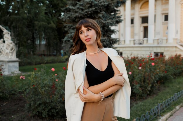 Mujer blanca de moda en chaqueta posando en la calle. Cabello ondulado, maquillaje natural.