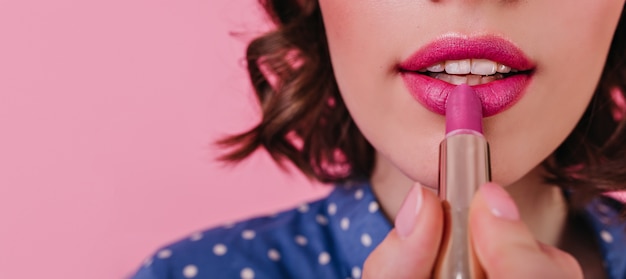 Mujer blanca sensual que hace su maquillaje antes de cita romántica. Toma de primer plano de ady rizado elegante posando en la pared rosa con lápiz labial.