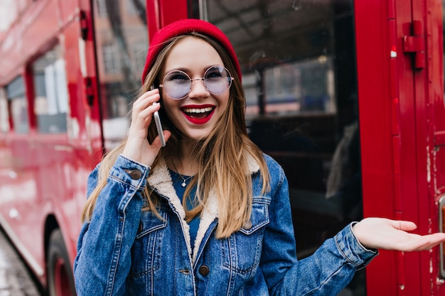Mujer blanca sorprendida con sombrero rojo hablando por teléfono.