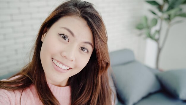 Mujer blogger asiática que usa un teléfono inteligente para grabar video vlog en la sala de estar en casa