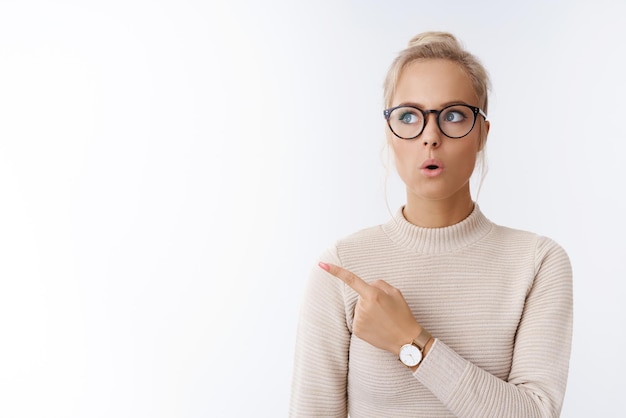 Mujer blogger social mirando hacia arriba apuntando hacia la esquina superior izquierda doblando los labios impresionado y aturdido por una idea impresionante en blanco