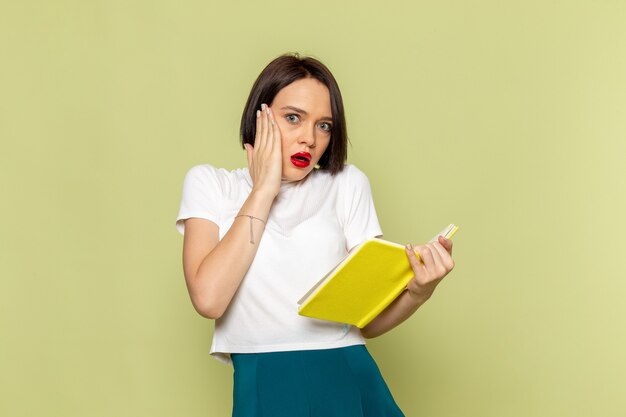 Mujer con blusa blanca y falda verde sosteniendo un libro amarillo y leyendo