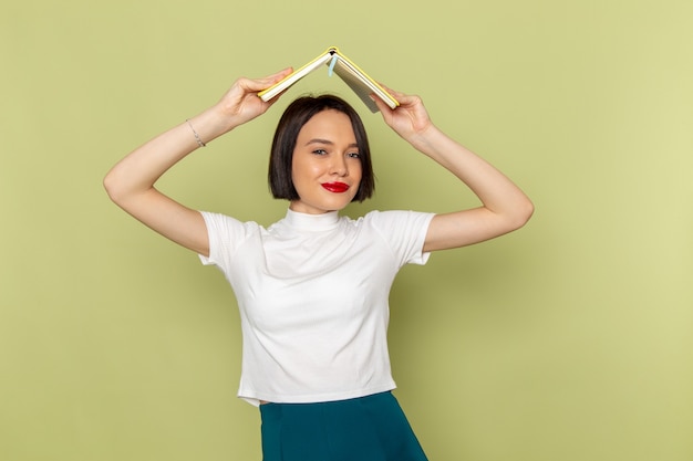 mujer en blusa blanca y falda verde sosteniendo libro