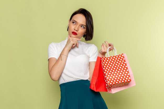 Mujer en blusa blanca y falda verde sosteniendo paquetes de compras con expresión de pensamiento