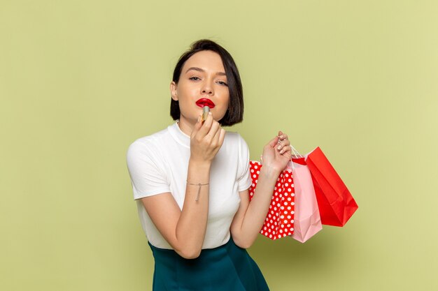 Mujer en blusa blanca y falda verde sosteniendo paquetes de compras y lápiz labial