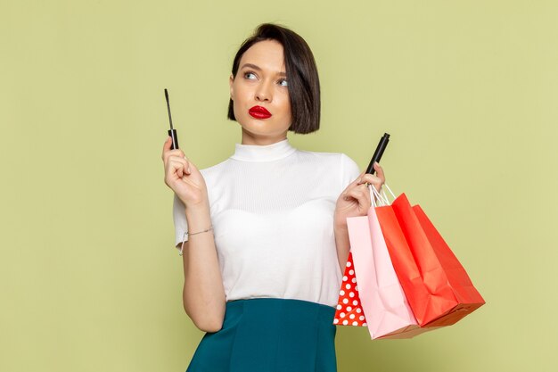 Mujer en blusa blanca y falda verde sosteniendo paquetes de compras y rímel