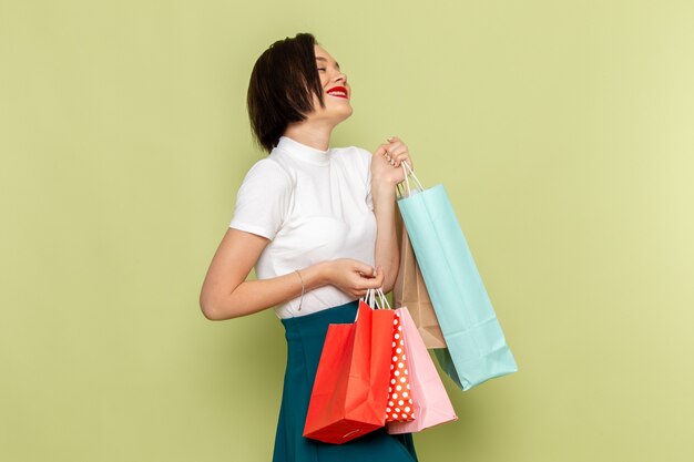 Mujer en blusa blanca y falda verde sosteniendo paquetes de compras con sonrisa y pose modelo de moda ropa femenina