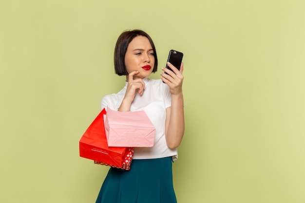 Mujer en blusa blanca y falda verde sosteniendo paquetes de compras y teléfono