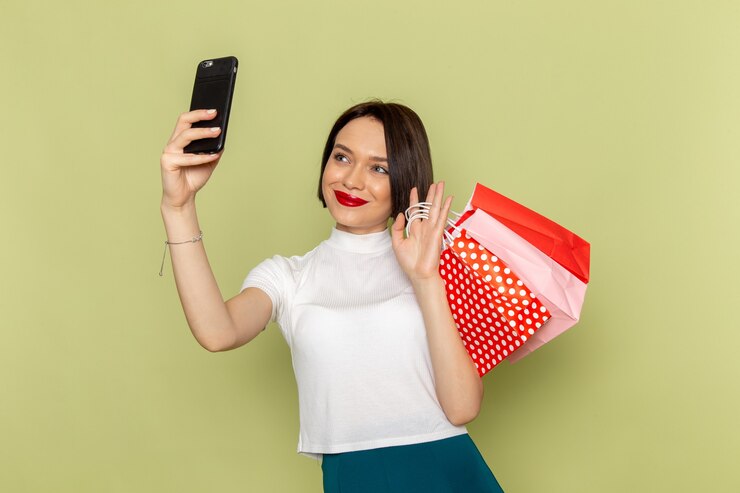 Foto gratuito mujer en blusa blanca y falda verde sosteniendo paquetes de compras tomando un selfie