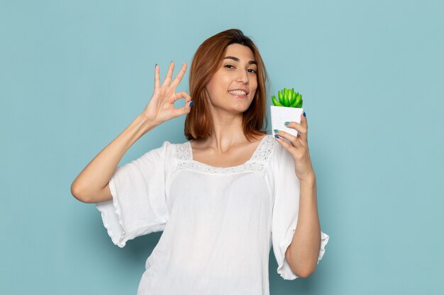 Mujer en blusa blanca y jeans sosteniendo una pequeña planta y sonriendo