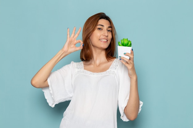 Mujer en blusa blanca y jeans sosteniendo una pequeña planta y sonriendo