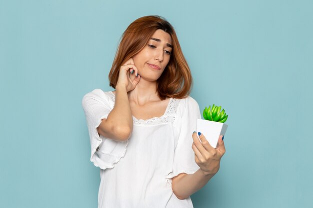 Mujer en blusa blanca y jeans sosteniendo una pequeña planta verde