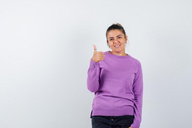 Mujer en blusa de lana mostrando el pulgar hacia arriba y mirando feliz