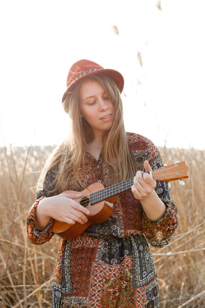 Mujer bohemia tocando el ukelele en el campo