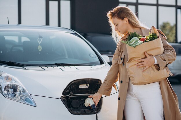 Mujer con bolsas de la compra de alimentos cargando coche eléctrico