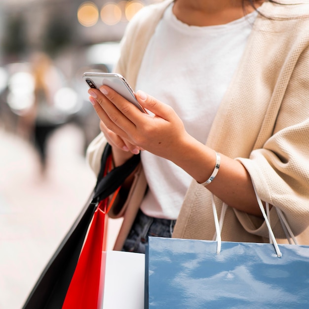 Mujer, con, bolsas de compras, mirar teléfono, aire libre