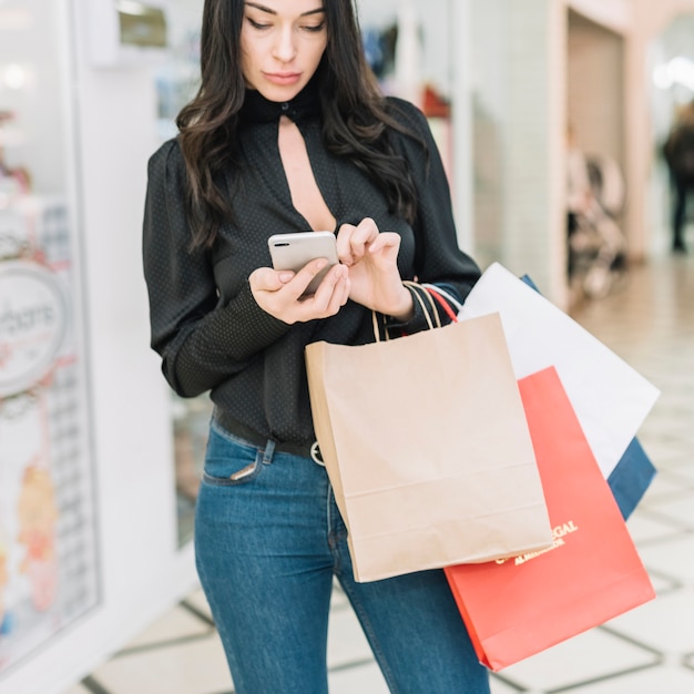 Mujer con bolsas de compras navegando smartphone