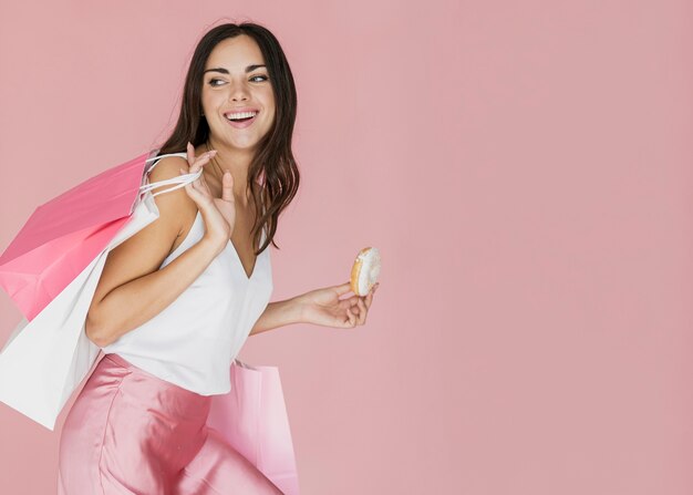 Mujer con bolsas de compras y una rosquilla sobre fondo rosa