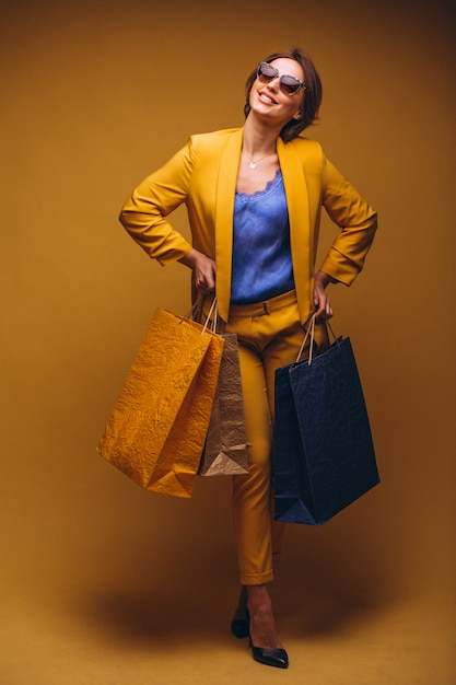 Mujer con los bolsos de compras en estudio en el fondo amarillo aislado