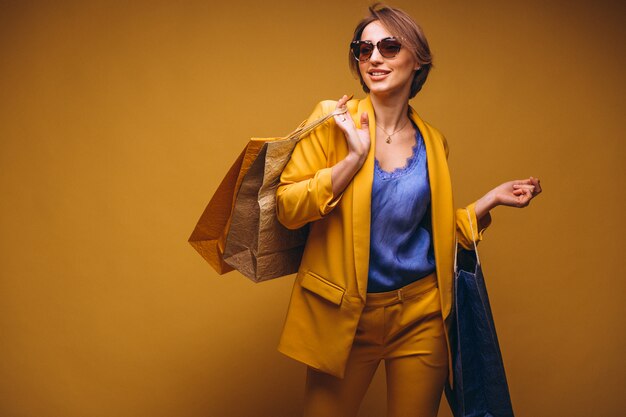 Mujer con los bolsos de compras en estudio en el fondo amarillo aislado