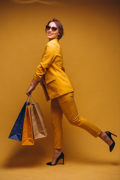 Mujer con los bolsos de compras en estudio en el fondo amarillo aislado