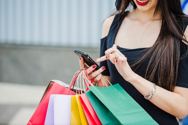 Mujer con los bolsos de compras que sostienen el smartphone