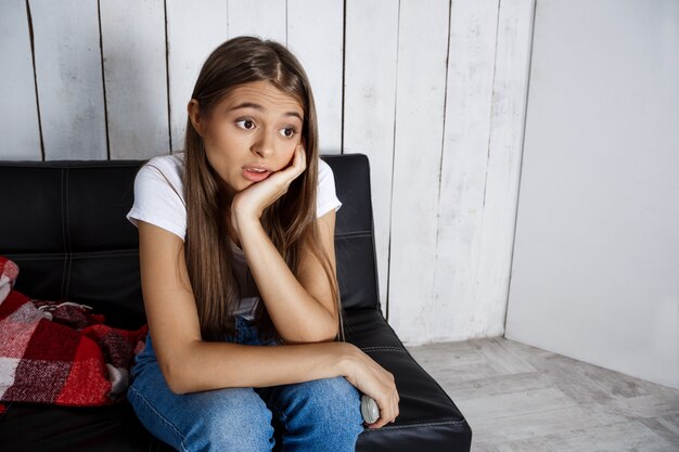 Mujer bonita aburrida viendo la televisión, sentado en el sofá en casa.