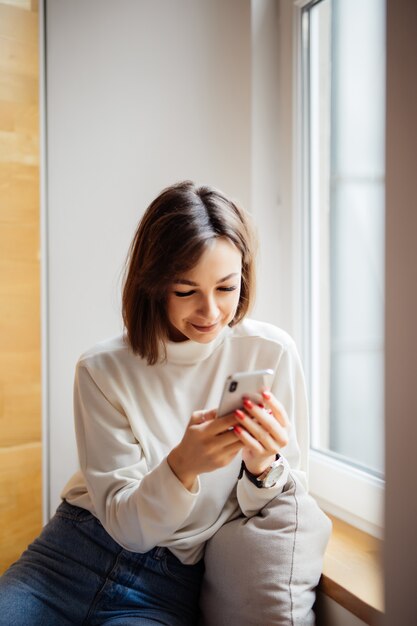 Mujer bonita adolescente interesada en camiseta blanca con mensajes de texto de teléfono inteligente