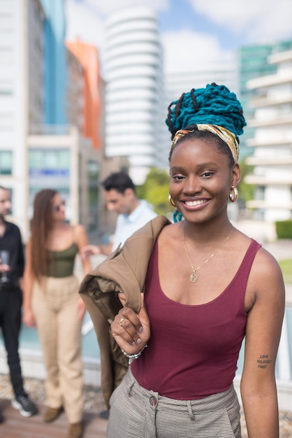 Mujer bonita afroamericana en fiesta en la azotea de la terraza. Mujer afroamericana de pelo largo en ropa casual. Personas de diferentes nacionalidades de pie en segundo plano. Teambuilding, concepto de fiesta