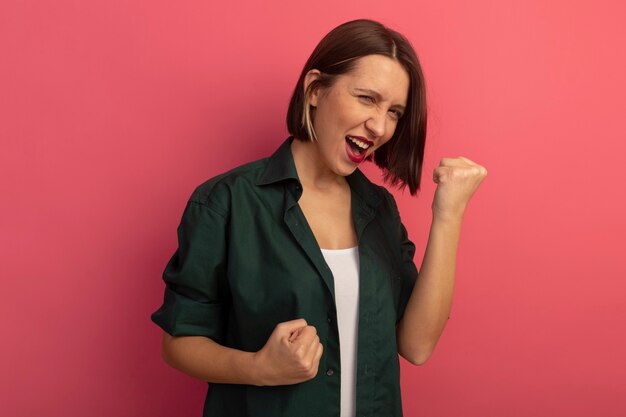 Mujer bonita alegre mantiene los puños mirando al frente aislado en la pared rosa