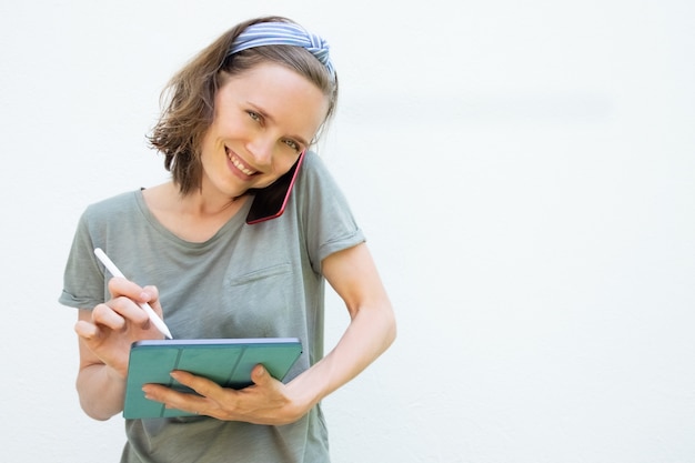 Mujer bonita alegre que usa la tableta y la pluma