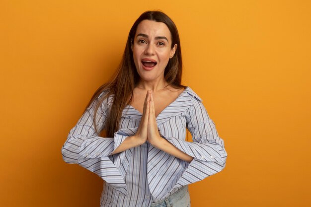 Mujer bonita alegre sostiene las manos juntas aisladas en la pared naranja