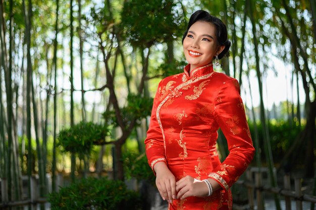 Mujer bonita asiática en vestido chino cheongsam tradicional con gesto de felicitación en el bosque de bambú
