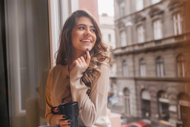 Mujer bonita blanca juguetonamente tocando la barbilla con el dedo mientras mira la ciudad