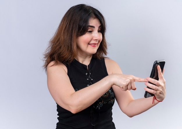 Mujer bonita en blusa negra apuntando al teléfono felizmente